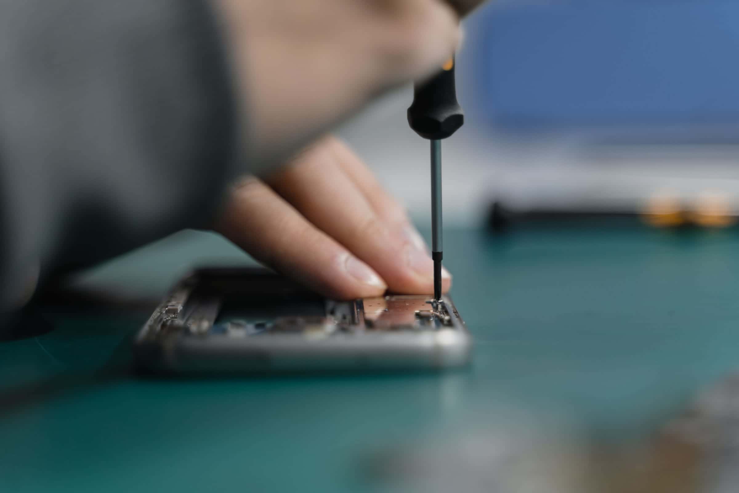 Mano desarmando un celular con un desarmador de precisión