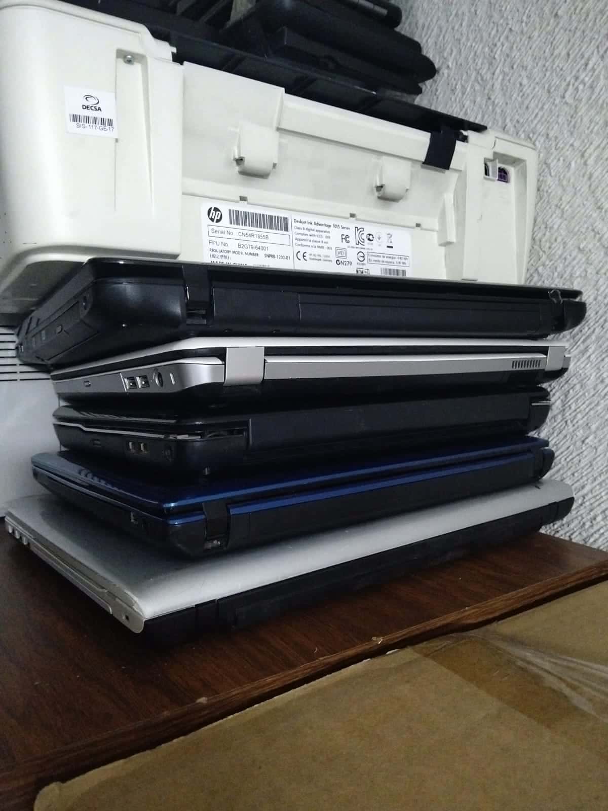 Laptops en desuso apiladas junto a una impresora, listas para reciclarse